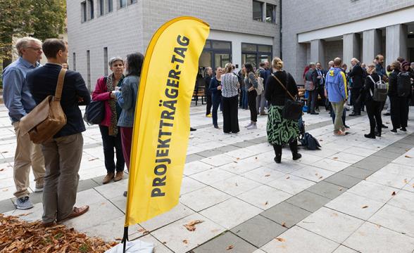 Viele Menschen gehen in eine Gebäude. Davor steht eine Flagge auf der steht: "Projektträger-Tag".