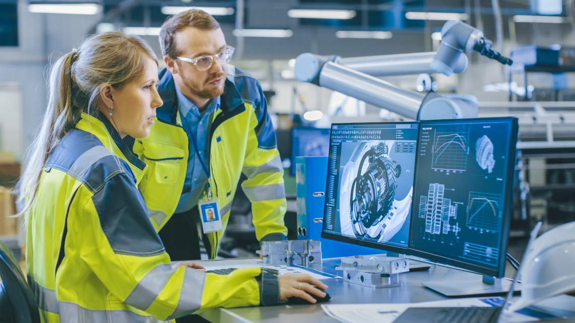 Frau und Mann arbeiten in einer Fabrik an einem Computer in Arbeitskleidung