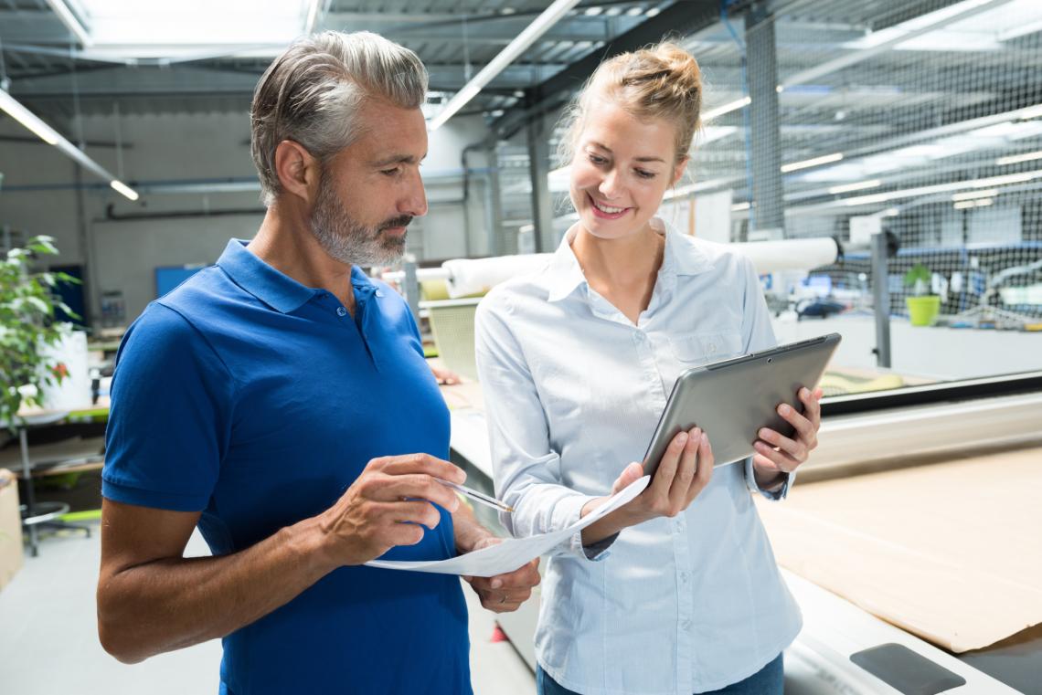 Mann und Frau mit Laptop und Papier in Logistikhalle